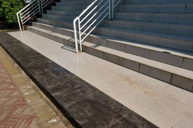 Pürüzsüz seramik yüzeyli fayanslı zemin ve merdiven, açık gri ve siyah renkler, beyaz korkuluklar ve güneş ışığını yansıtan hafif toprak izleri..