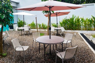 Sandalyeler ve masalar parkta şemsiyelerin altında görülür..