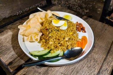 Bir tabak Endonezya usulü kızarmış pirinç (nasi goreng) dilimlenmiş salatalık, domates, haşlanmış yumurta, fıstık, kraker ve bir parça limon ile servis edilir..