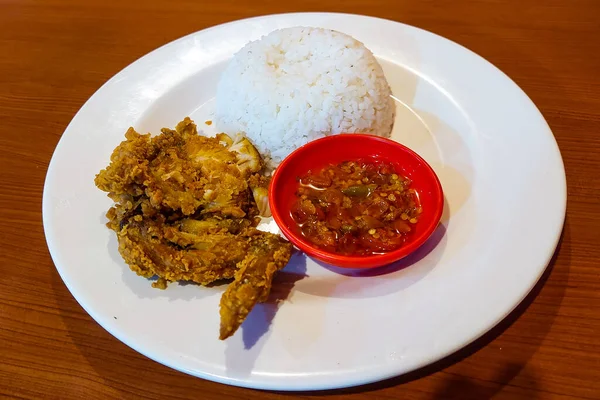 Pirinç, tavuk ve biber sosu ahşap bir masada beyaz bir tabakta.