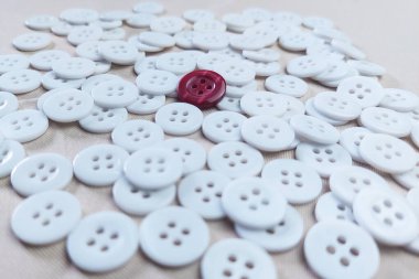 Etrafa saçılmış bir sürü beyaz düğme ve kumaş dokusunda kırmızı bir düğme var..