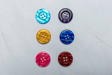 Renkli düğmeler beyaz bir kumaş üzerinde düzgünce düzenlenir..