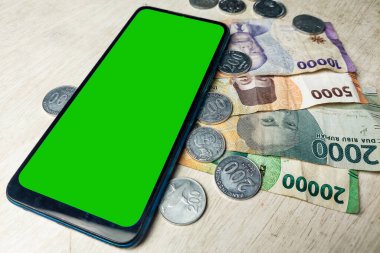 Banknotlar, madeni paralar ve cep telefonu yeşil ekranı beyaz masada