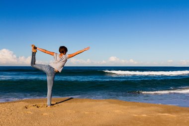 Genç kadın bir kumsalda Yoga yapar
