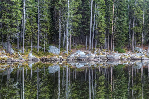 Ağaçları ve kayaları sakin gölde yansıyan