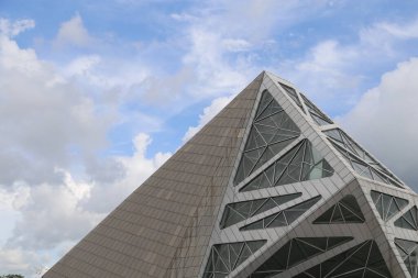 a tall, triangular building with angular lines and large windows against the blue sky. the structure is made of gray metal tiles and features an intricate geometric design that forms sharp angles at its edges