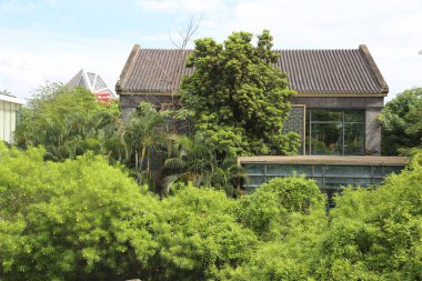there is an old chinese-style building with green plants growing on the roof and walls. the house has two floors of glass windows, surrounded by lush trees in front of it