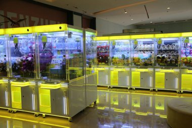 a large room with numerous claw machine cabinets, each cabinet is yellow and white in color. the walls of the cabinets have glass panels decorated with colorful flowers and plush toys inside them