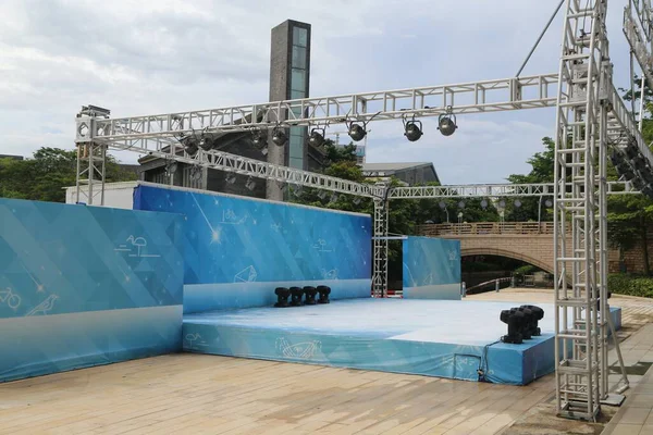 a large outdoor stage with blue and white silk on the sides, a truss structure for lighting, led screens above it, and silver steel handrails at each side of the main entrance area.