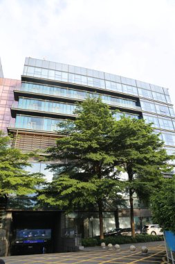 Bina modern, girişinin önünde cam perdeler ve ağaçlar var. Zemin katta bir tarafta ofis ve aşağıda araçlar için park yerleri var..