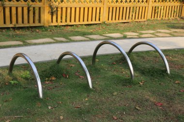 Paslanmaz çelik bisiklet rafları, basit ve zarif bir dizaynda üç kemer, açık hava oyun parkının önündeki çimenliğe yerleştirilmiş ahşap parmaklıklar.