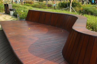 Açık hava koyu kahverengi parke döşemesi üzerine kurulmuş, tahta çatal şeklinde bir ahşap bank. Bahçe bahçesinde ya da park alanında, yeşillik ve diğer banklarla çevrili..