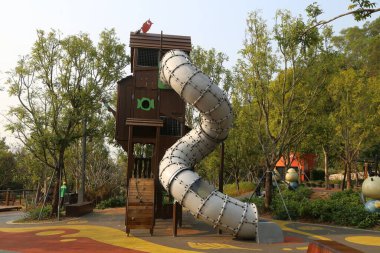 Bir kaydırak ahşap ve metalden yapılır. Bir parkta yer almaktadır. Arka planda ağaçlar var.