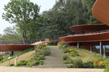 Yeşil tepesi ve merdivenleri olan büyük bir bina. Binanın birçok penceresi var ve çevresi bitkilerle çevrili.