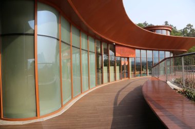 Dışarıdaki ahşap bir güvertedeki eğimli cam perde duvarı, büyük düz bakır levhalar ve güneş ışığını korumak için metal çerçeveler. Binanın dış tarafında turuncu-kırmızı duvarlar var. Yeşilliklerle çevrili. Eşsiz bir mimari stil yaratıyor.