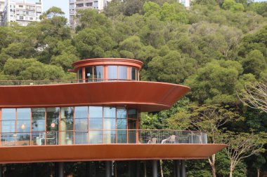 Geniş pencereli ve balkonlu bir bina. Balkon en üst katta. Bina ağaçlarla çevrili.