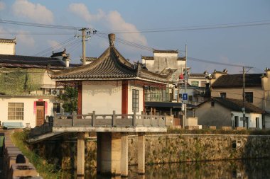 Çin kırsalındaki eski bir nehrin kıyısında, beyaz duvarları ve kırmızı fayansları olan, diğer evlerle çevrili küçük, antik bir Çin binası. Binaların simetrik mimarisi ve geleneksel bir tarzı var.