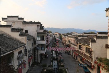 Her iki tarafında beyaz duvarlar ve siyah fayanslar olan antik bir kasabadaki şehir caddesi manzarası hizalanmıştır. Etrafta alışveriş yapan çok insan vardı.