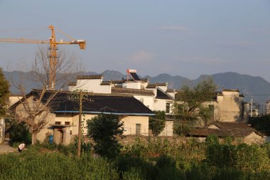 Bir kasabanın arka planında bir vinç var. Vinç sarı. Kasaba dağlarla çevrili.
