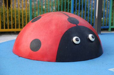 Çocukların oyun parkında oynaması için uğurböceği şeklinde bir kubbe. Vücudunda büyük gözler ve siyah noktalar var. Açık havada mavi asfalt üzerine yerleştirilmiş.