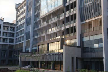 Yeni binanın dış kısmında, gri duvarlar ve beyaz cam perdeli pencereli kentsel bir tarz yer alıyor. Ön cephe güneş ışığını korumak için bir tarafta tahta çıtayı içerirken, somut elementler görüntüsüne görsel derinlik katıyor.