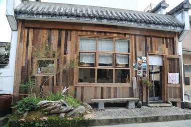 Önünde bank olan ahşap bir bina. Bank taştan yapılmıştır. Binanın önünde saksı bitkisi var.