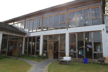 İki katlı binanın dış yüzeyi beyaz duvarlar ve ahşap pencerelerden yapılmış. Birinci kattaki büyük cam kapılar içerideki eşyaları gösteriyor..