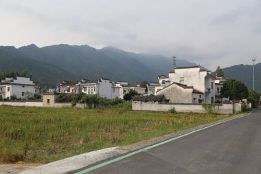 Uzakta, geleneksel Çin mimarisi tarzında yeşil pirinç tarlaları ve kırsal Çin 'deki dağlarla çevrili antik beyaz duvarlı bir ev var.