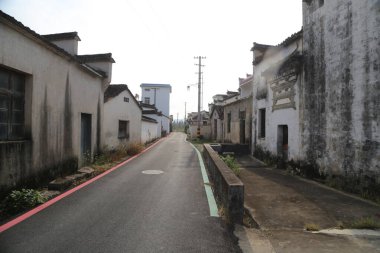 Asfalt yol eski köyden geçiyor, her iki tarafında beyaz duvarlar ve siyah fayanslar var. Her evin önünde açık bir alan var, aralarında yeşil çimenler büyüyor.