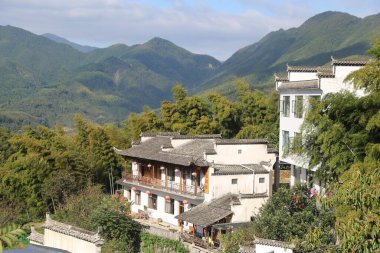 Dağlık bölgede yeşil dağlar ve ağaçlarla çevrili bir grup beyaz bina. Binalar eski Çin mimarisidir. Sade saçakları, tahta duvarları, ahşap kapıları ve pencereleri vardır. Manzaralı manzaraya bakarlar.