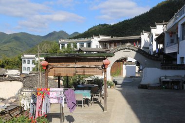 Çin 'in güneyindeki dağlarda beyaz duvarları ve iki katlı binalarda siyah fayansları olan kırsal bir avlu. Bir uçta başka bir binaya açılan bir kemer var..