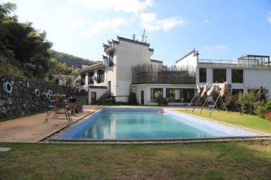 Üst katında beyaz duvarları ve siyah fayansları olan eski bir Çin tarzı iki katlı villa var. Zemin katta yeşil çimlerle çevrili bir yüzme havuzu ve yanında da çocuk oyuncakları var..