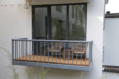 Gri metal parmaklıkları, ahşap döşemeleri ve cam kapıları olan basit bir balkon. Balkon, modernist mimari tarzda bir apartmanın birinci katında yer almaktadır..