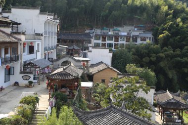 Beyaz duvarları ve siyah kiremitleri olan eski bir Çin tarzı binanın manzarası. Köy yeşil dağlar ve bambu ormanlarıyla çevrili.