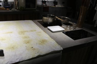 Mutfak tezgahının üzerine büyük bir parça beyaz kağıt konur. Yanında tencere tava ve tencere ve tencere ile dokunmuş yağdan bulaşmış sarımsı lekelerle lekelenir.