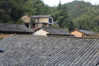 Çin kırsalındaki eski evin çatı kiremitleri, tepeden bakıldığında gri ve siyah taş tuğlalardan yapılmıştır. Önünde, hepsi farklı renkte kiremitli çatılara sahip birkaç ev daha bulunuyor..
