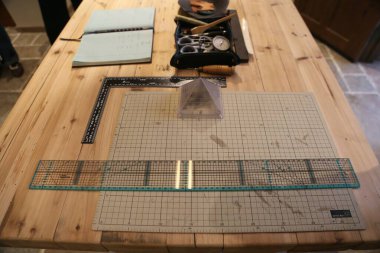 Endüstriyel dikiş stüdyosu. Masanın üzerinde geniş, akrilik ızgaraya benzeyen düz çizgiler ve farklı boyutlarda noktalar var. Cam karolar üzerinde desenler oluşturmak için kullanılıyor..