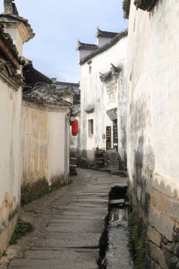 Beyaz duvarları ve gri kiremitleri olan eski bir Çin köyünde küçük bir sokak. Sol tarafında bir ırmak var, su da akıyor. Sokağın her iki tarafında da siyah ahşap yapı ve taş tuğlalardan yapılmış evler vardı.
