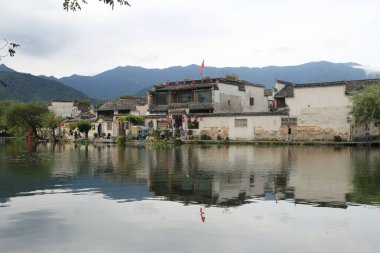 Anhui, Çin 'de küçük bir köy, suyun kenarında, antik mimari ve dağlarla çevrili. Binalar çatılarından sarkan kırmızı bayraklar taşıyor..
