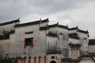 Çin tarzında beyaz duvarlı, siyah kiremitli bir bina. Anhui ilinin wuyuan köyünde yer alıyor. Duvarlarda kırmızı fenerler asılı ve tepemizde gri bir gökyüzü beliriyor..