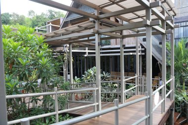 Yeşillik ve modern mimari ile çevrili Amanpura Chiang Mai Oteli 'nin açık hava alanında yüksek bir yürüyüş yolu olan ahşap ve çelik bir gölgelik..