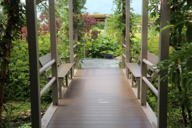 Evinizin girişine giden ahşap yolun her iki tarafında da yemyeşil ve egzotik bir bahçe tarzında beyaz metal parmaklıklı bitkilerle çevrili iki bank var..