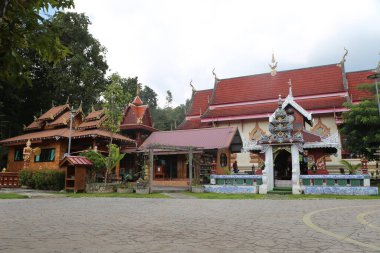 Eski Tayland tapınağı binasının önü, duvarlarında karmaşık oymalar olan ahşap binalarla çevrili kırmızı ve beyaz kiremitlerle süslenmiştir..