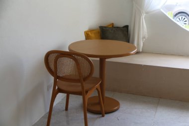 Pencerenin önünde iki sandalyeli, basit ve modern tarzda küçük yuvarlak bir masa. Açık kahverengi ahşap renkler ve her iki taraftaki rattan sırtüstü sandalyeler rahat bir atmosfer yaratır.