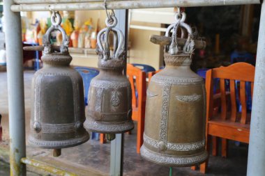 Phuket, Tayland 'daki kapalı bir pazarın tavanında asılı üç büyük bronz çan. Arka plan bulanık ve bir tarafında renkli sandalyeleri gösteriyor.