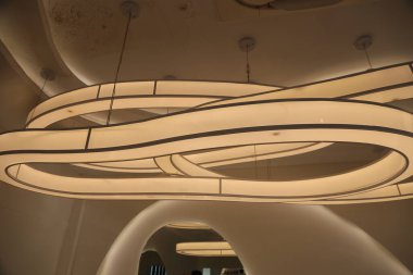 Ortasında iki büyük kıvrımlı lamba armatürleri olan beyaz bir tavan. Işıklarda siyah çizgiler ve kıvrımlar var..