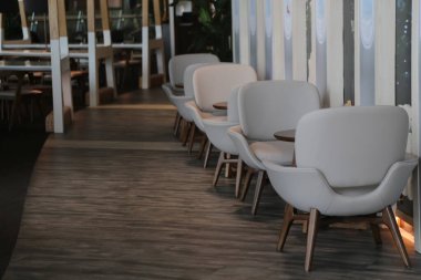 Bir havaalanı lobisinin köşesinde, tahta bacakları ve beyaz deri koltukları olan bir sıra modern sandalye. Arka planda koyu ahşap döşemeden yapılmış bir zemin var.