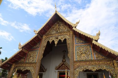 Chiang Mai 'deki tapınağın dışı, beyaz bulutlarla çevrili altın ve mavi süslemelerle süslenmiştir. Ana yapı geleneksel Thai mimari tarzına sahiptir, çatısında ve duvarlarında karmaşık desenler vardır.