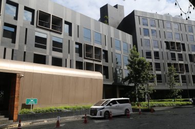 modernist tarzda bir otel binası, gri duvarları ve beyaz pencereleri olan ön cephe manzarası. Girişe yakın bir yerde park edilmiş bir araba var.