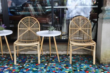 Renkli mozaik zeminde yuvarlak masalı bir çift rattan sandalye, açık hava kahve dükkanının penceresinin önüne yerleştirilmiş. Sahne arkadan çekiliyor ve rahatlatıcı bir atmosfer yayıyor..